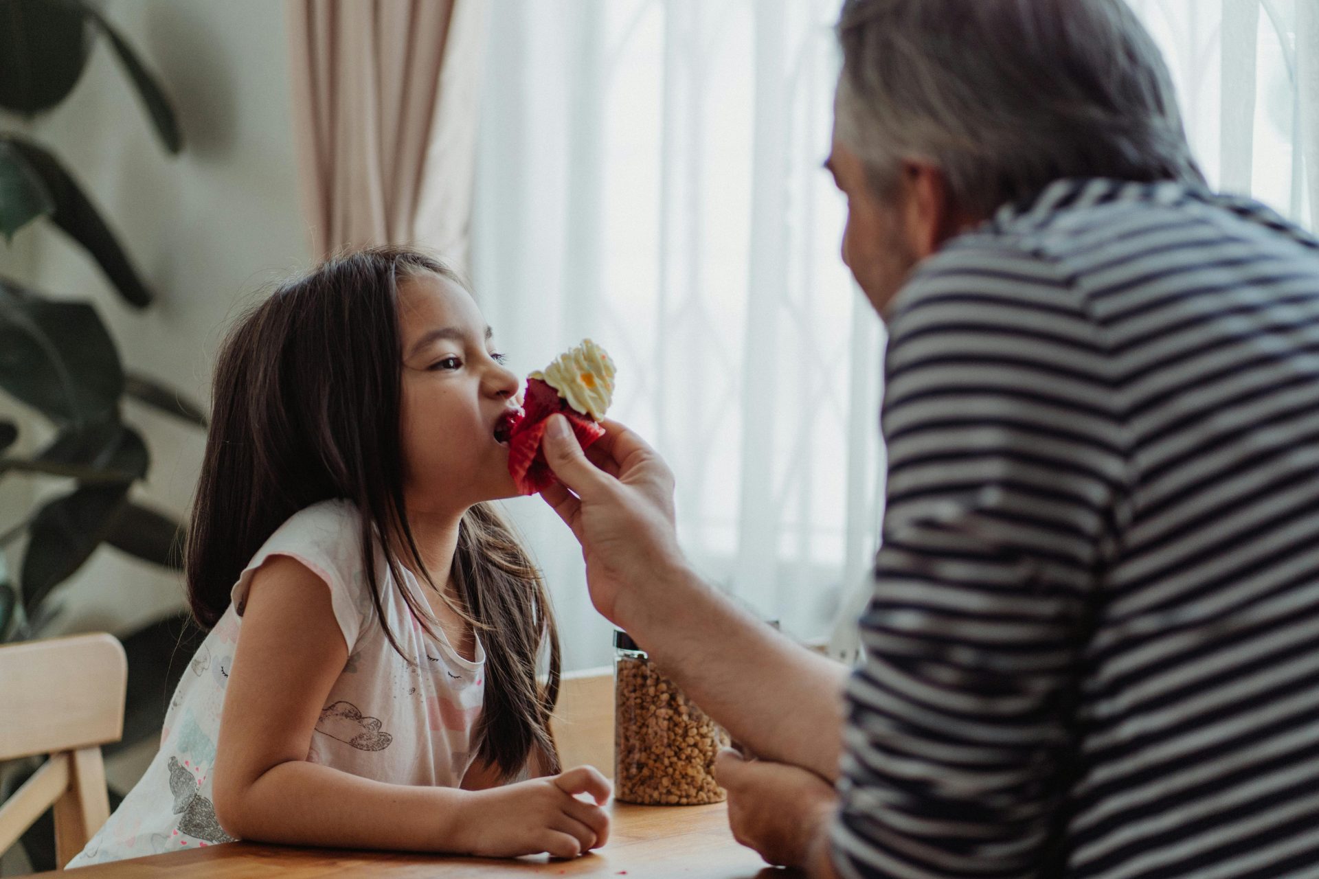 Grandfather sharing a cupcake with his granddaughter at the kitchen table, symbolizing family moments supported by thoughtful retirement planning.