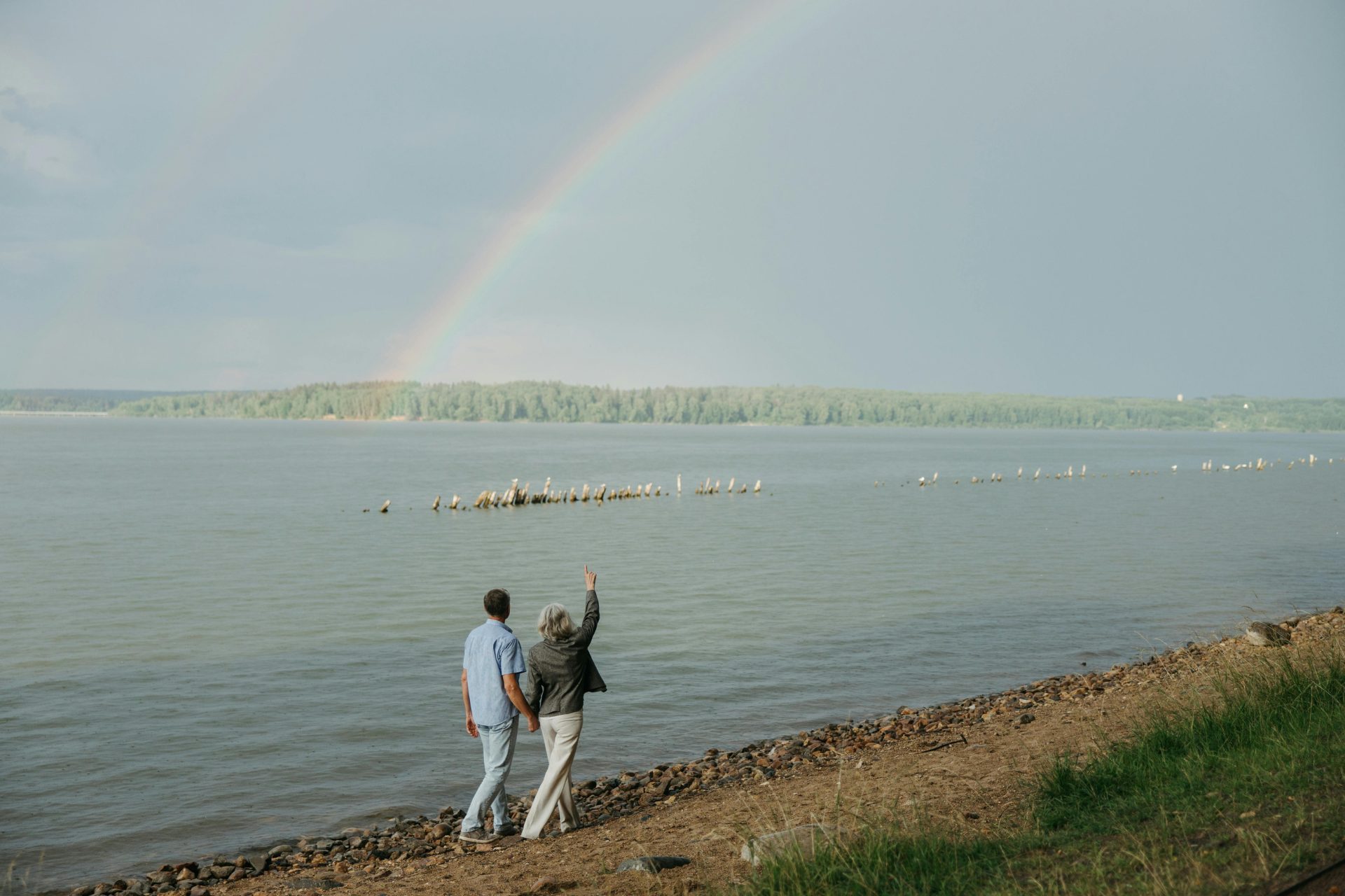 Two adults walk on a shoreline under a rainbow to discuss how much can I spend in retirement.